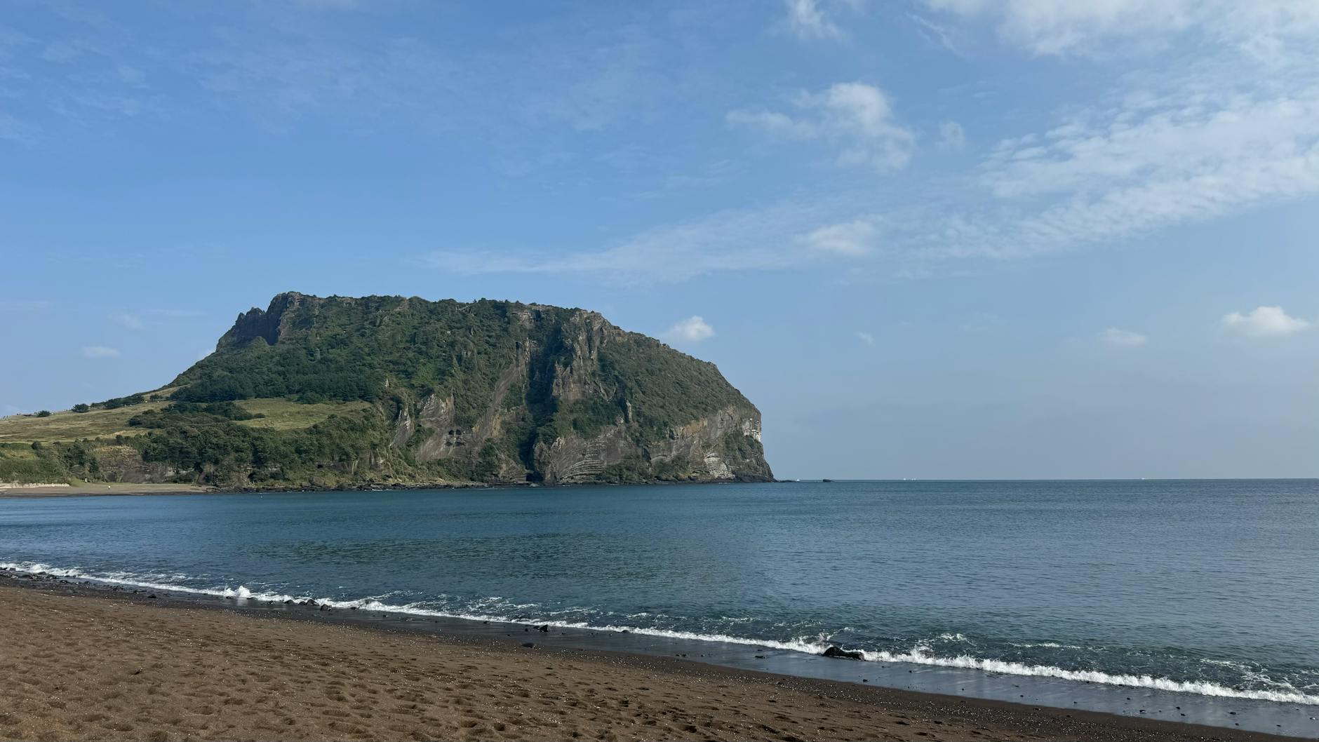 Peaceful beach view with Seongsan Ilchulbong peak on Jeju Island, South Korea.