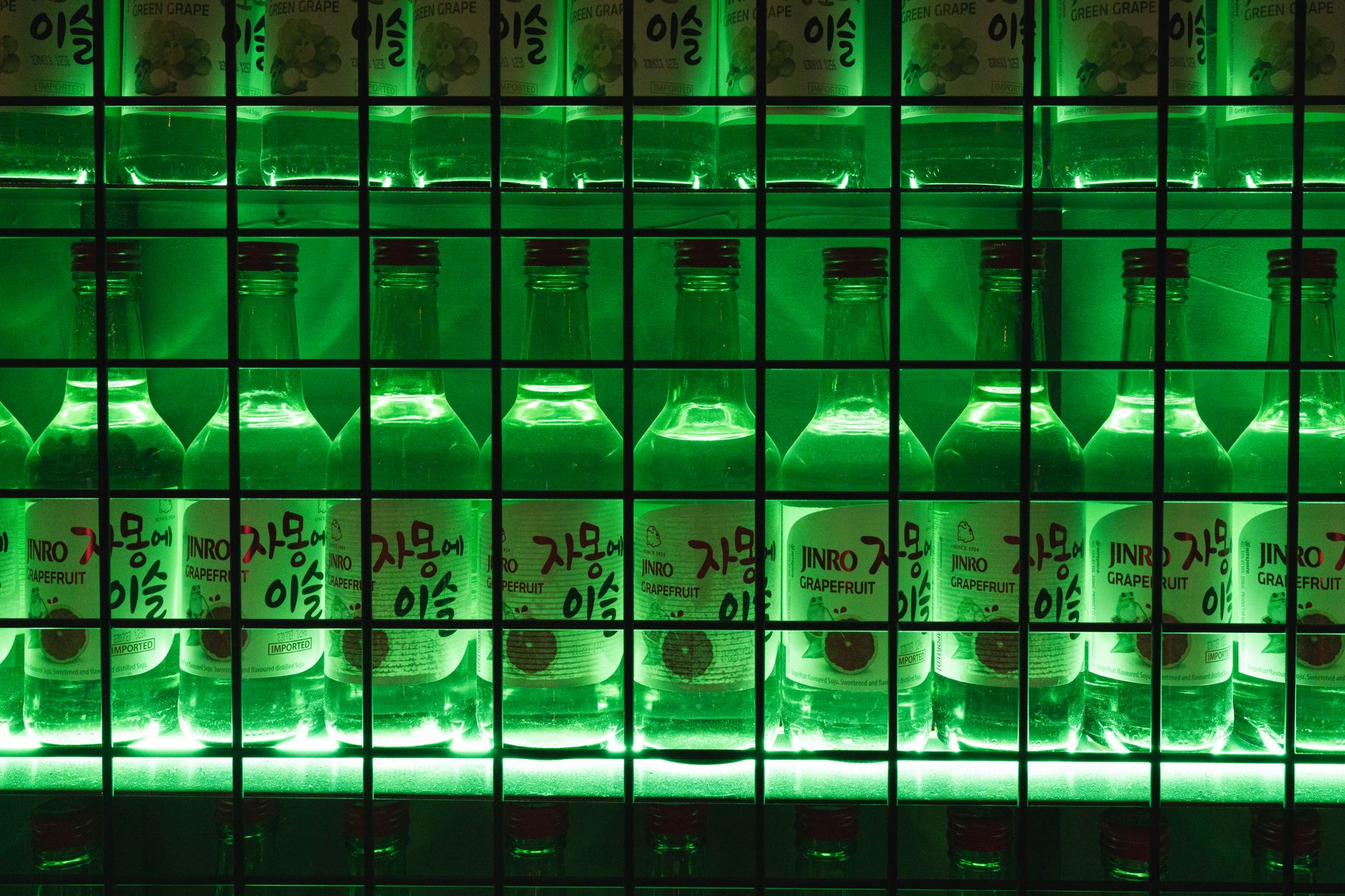 Illuminated bottles of Jinro Grapefruit soju on a vibrant green-lit shelf, creating a bold and artistic display.