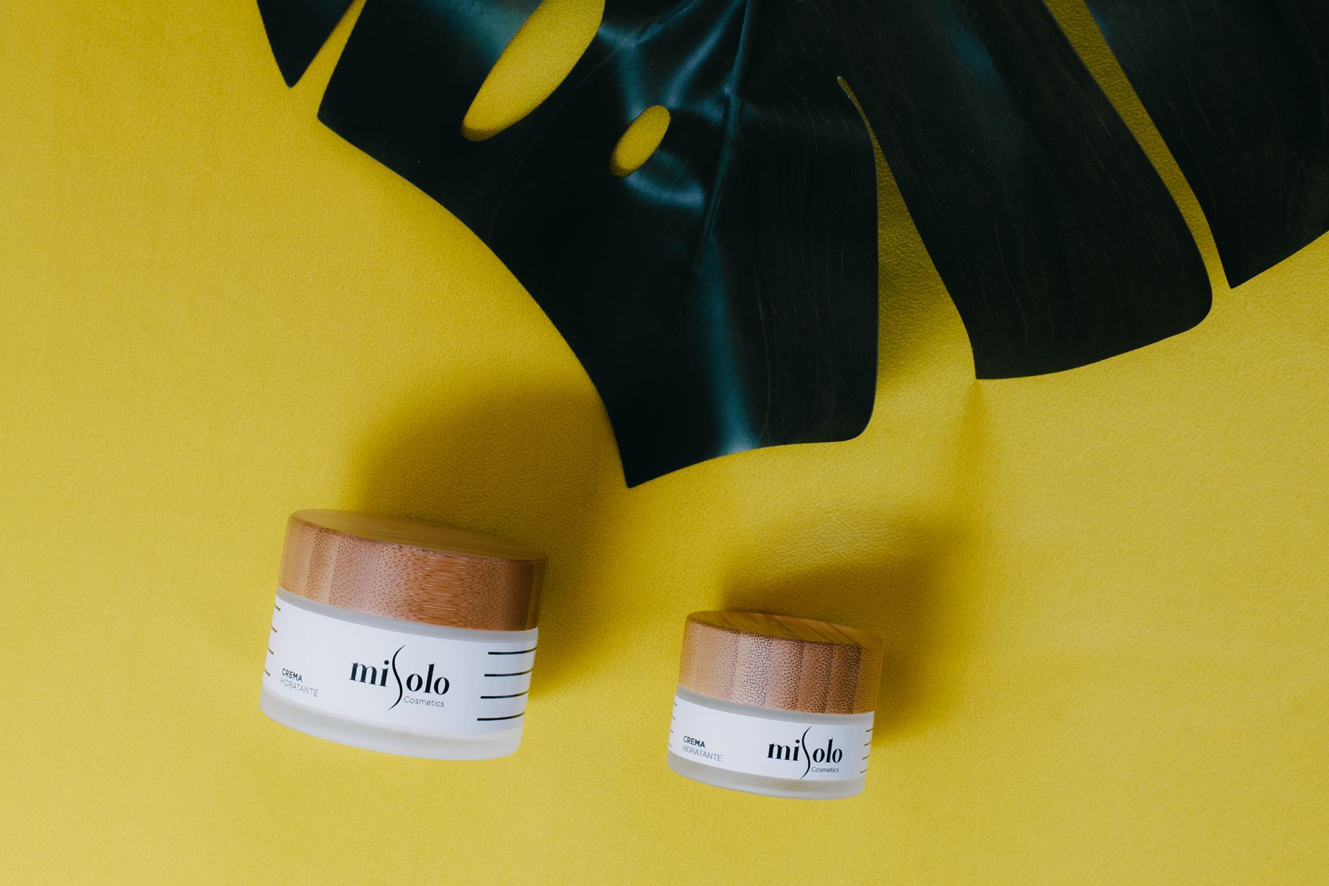 Flatlay of misolo skincare products with wooden lids on a vibrant yellow background with green leaf.