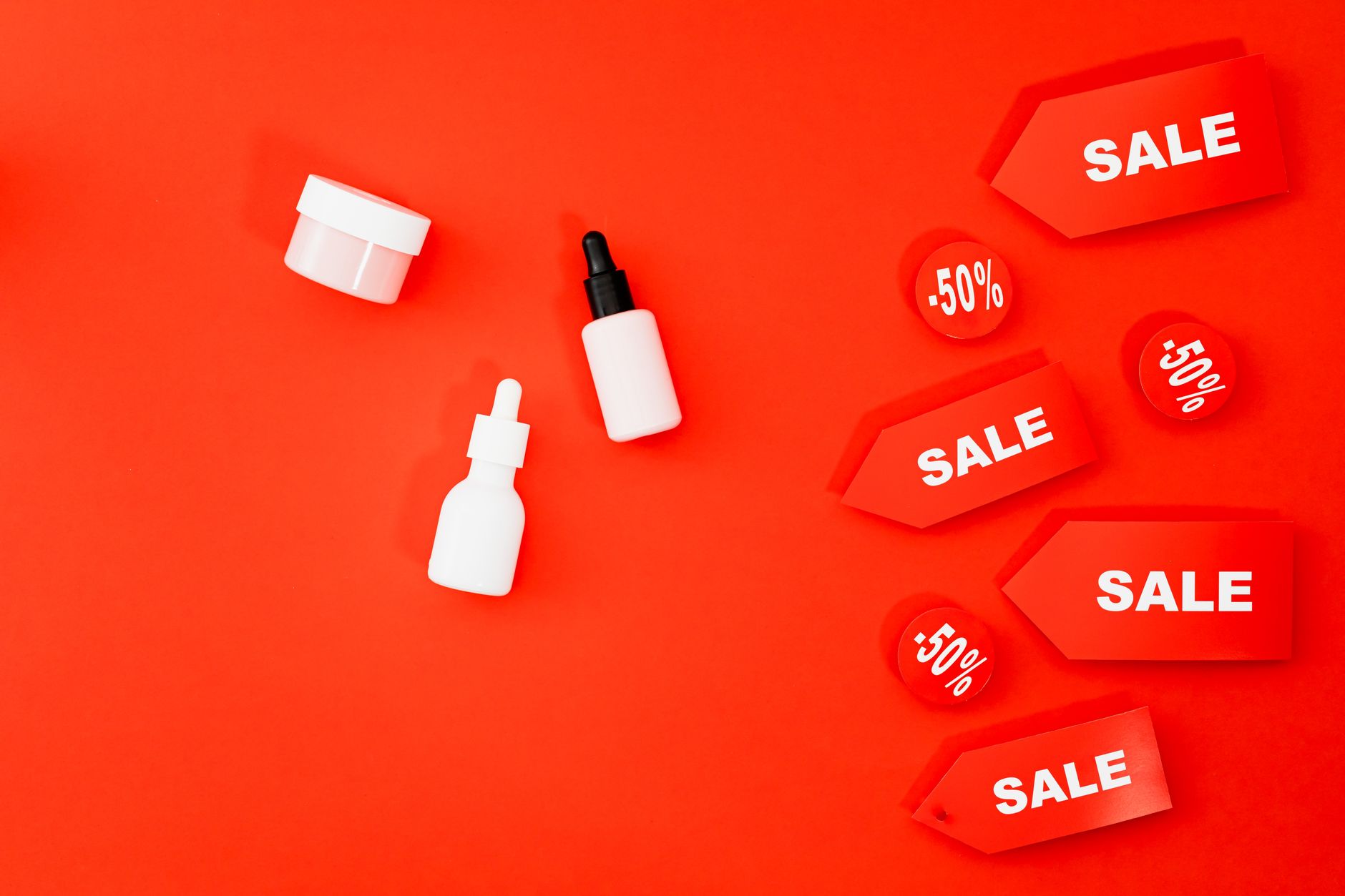 Flat lay of beauty products and sale tags on vibrant red background.
