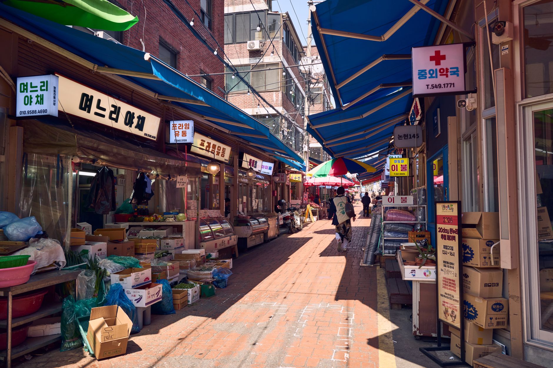 Bustling outdoor market in Seoul with colorful stalls under blue awnings.