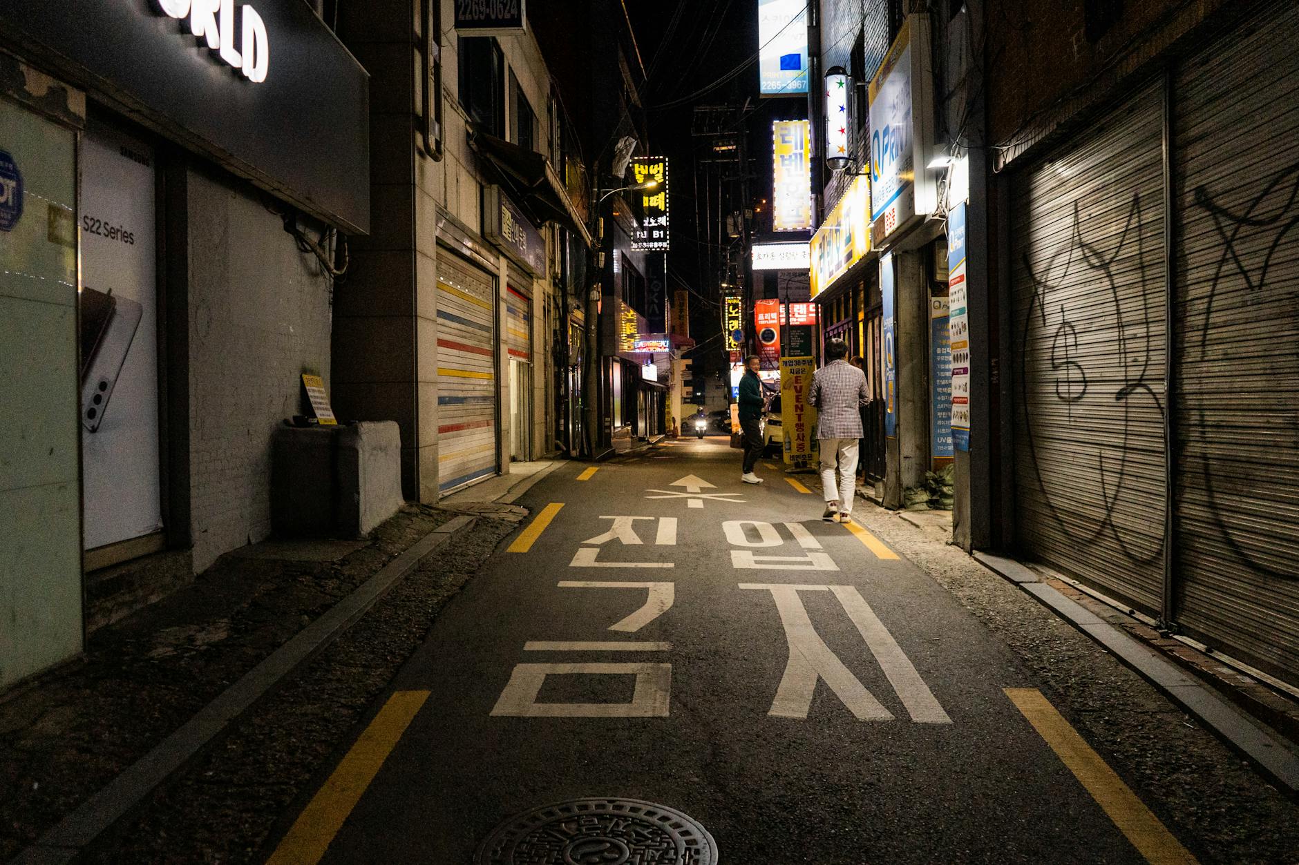Nighttime urban scene in a narrow street of Seoul, showcasing vibrant city life and architecture.