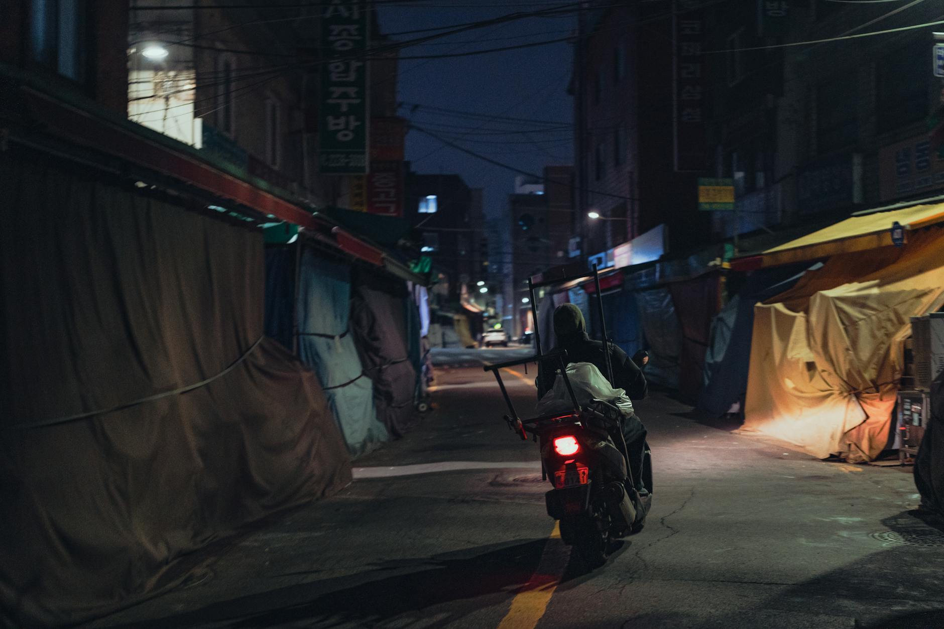 Moody night-time view of a motorcyclist navigating through Seoul's quiet alleyways.
