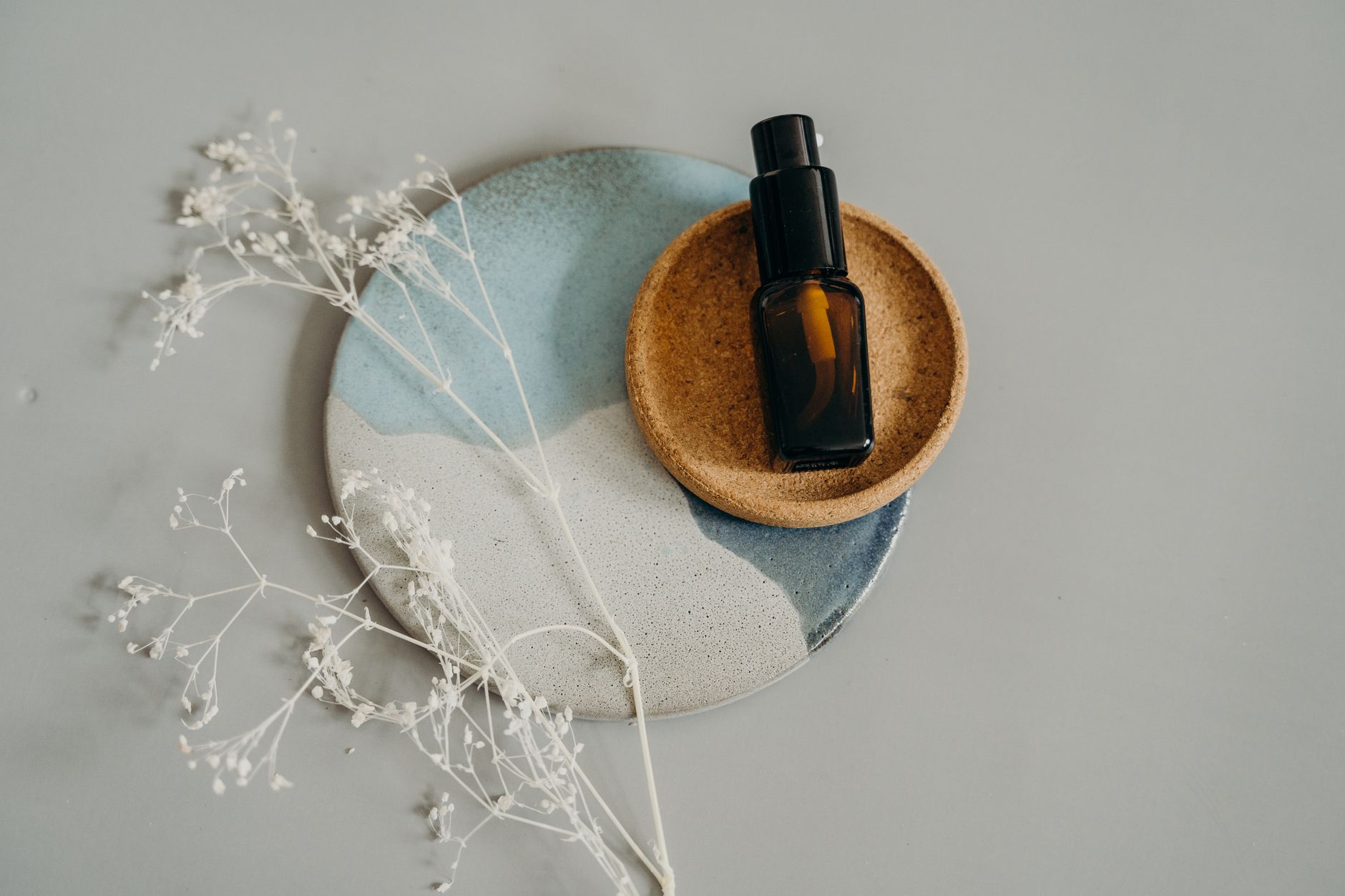 Stylish flatlay of a cosmetic bottle on ceramic plates, accented by delicate dried flowers.