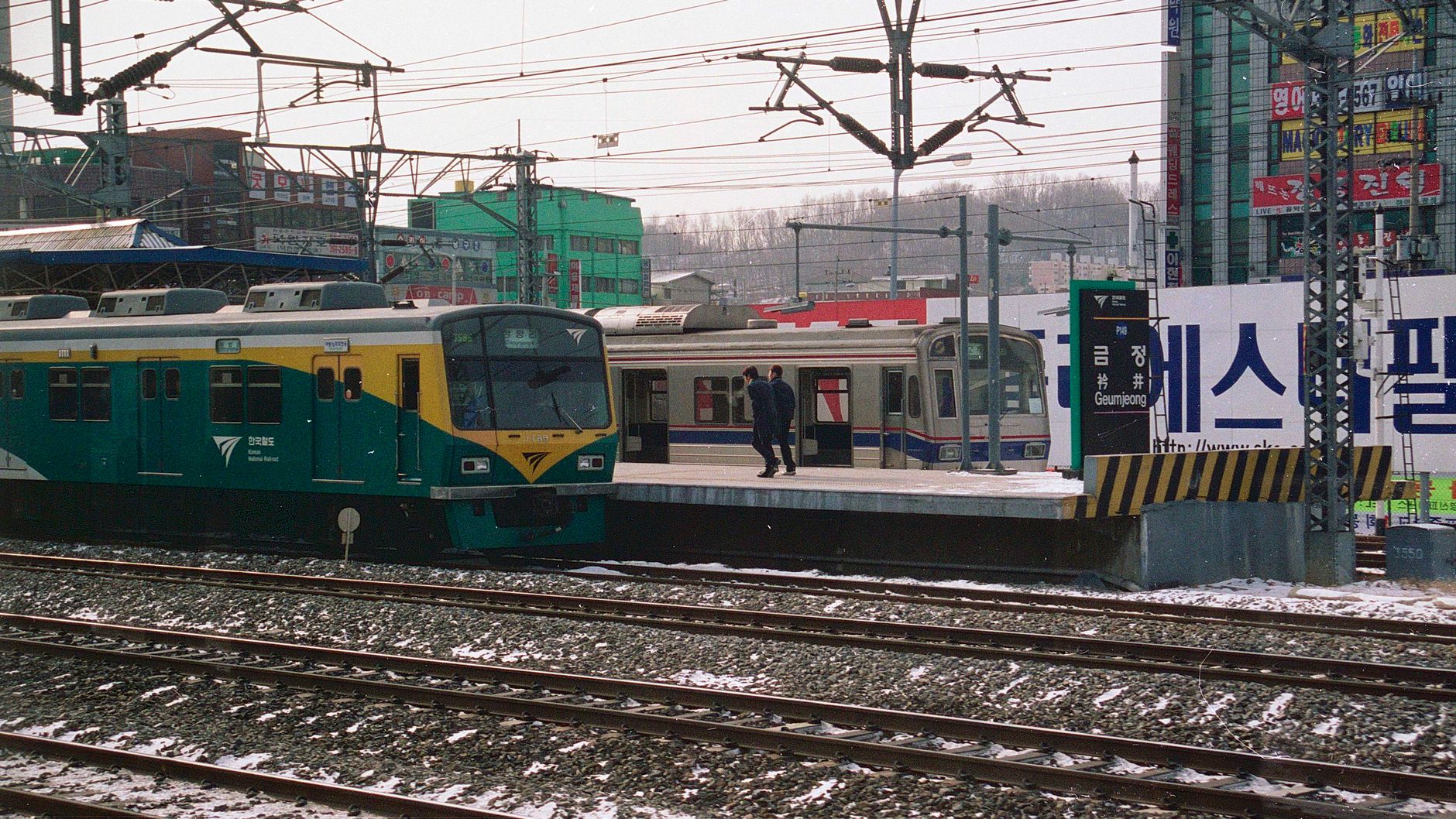Snowy day at Geumjeong train station with two trains and passengers in South Korea.