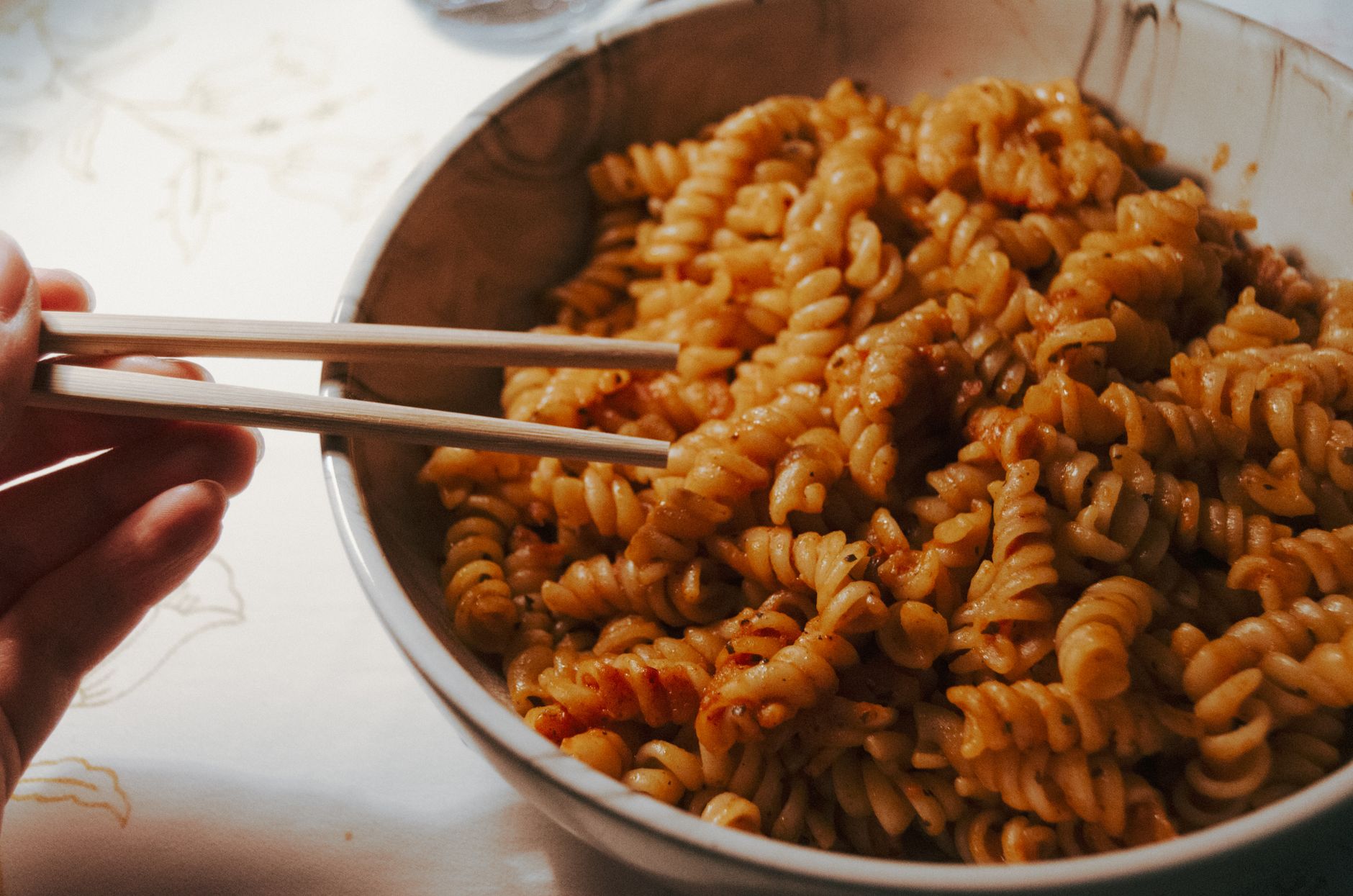 Fusilli pasta served in a bowl, enjoyed using chopsticks, creating a fusion cuisine experience.