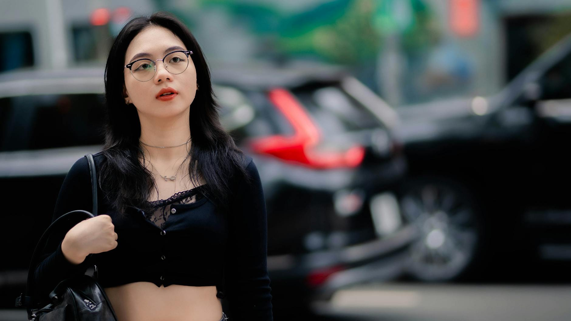 Chic Asian woman with eyeglasses in urban street, showcasing modern fashion style.
