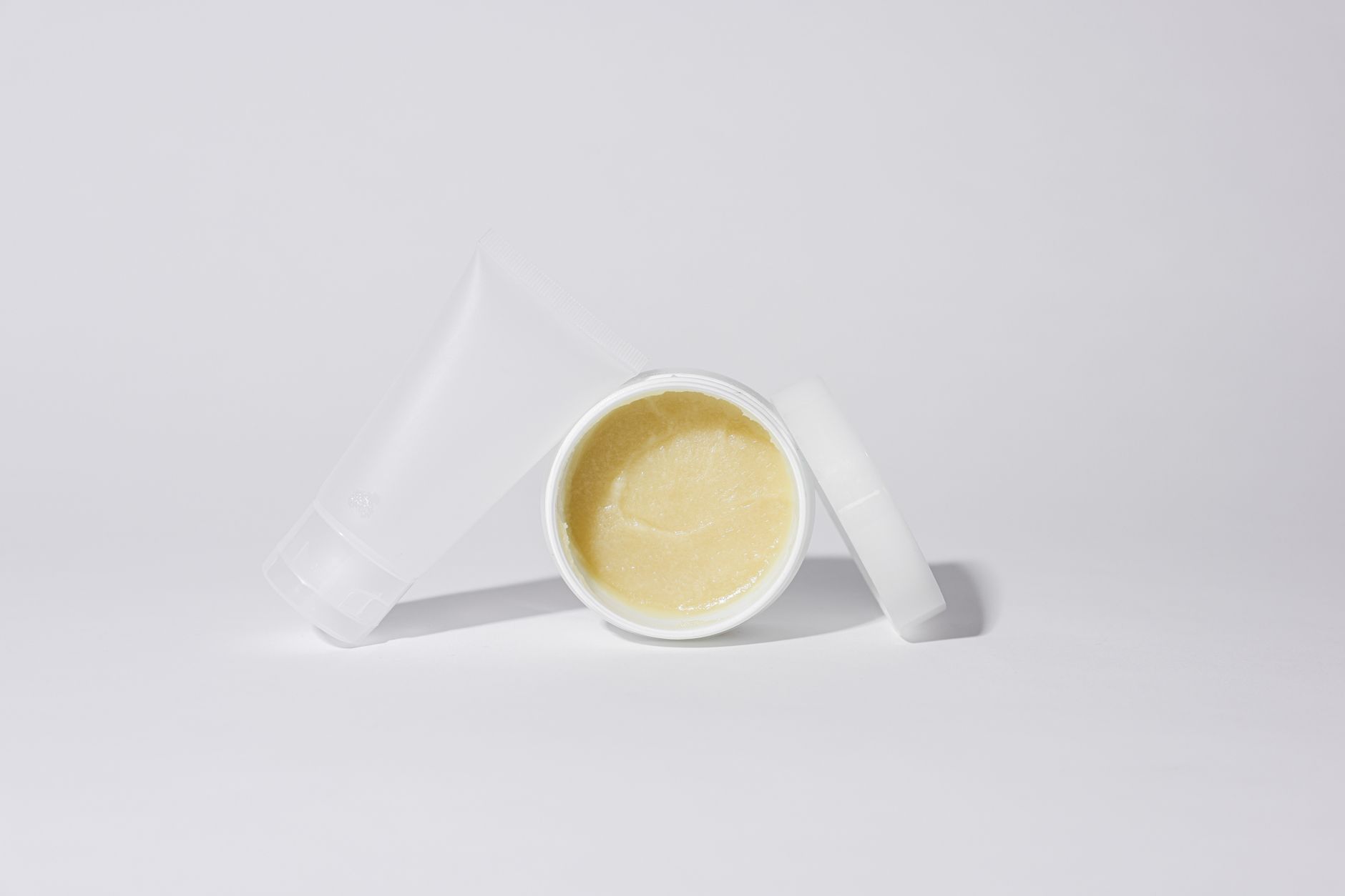 Studio shot of white plastic containers with yellow cream product on a white background.