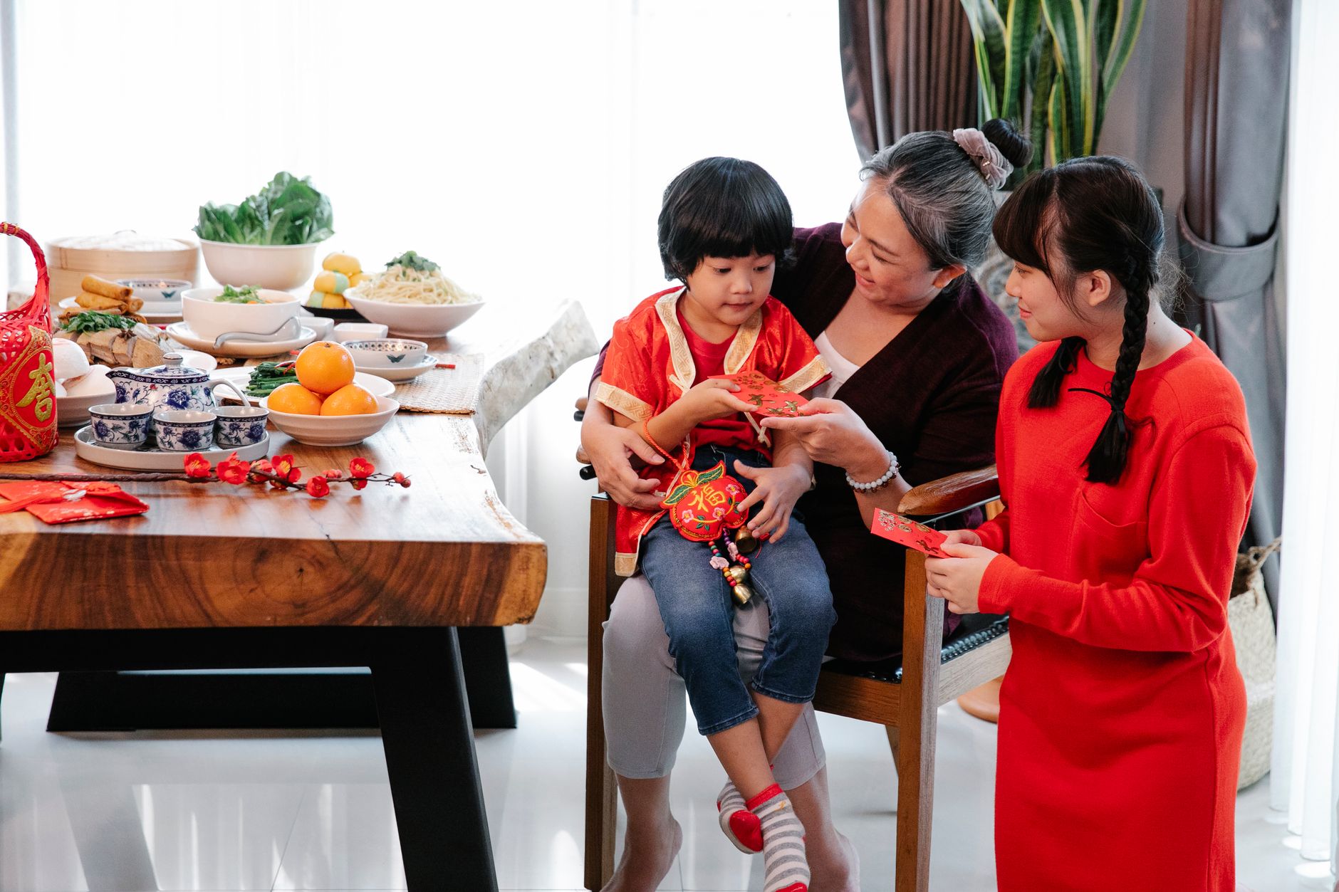 Happy Asian grandmother and presenting greeting card to grandson while celebrating New Year with grandchildren at table with Chinese dishes