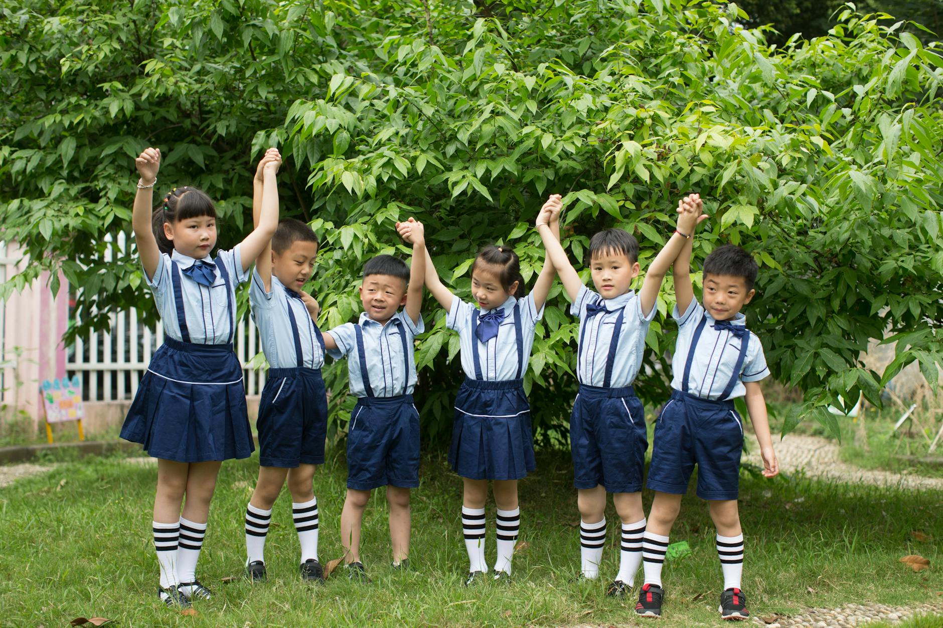 Group of Asian children in uniforms holding hands and celebrating outside.