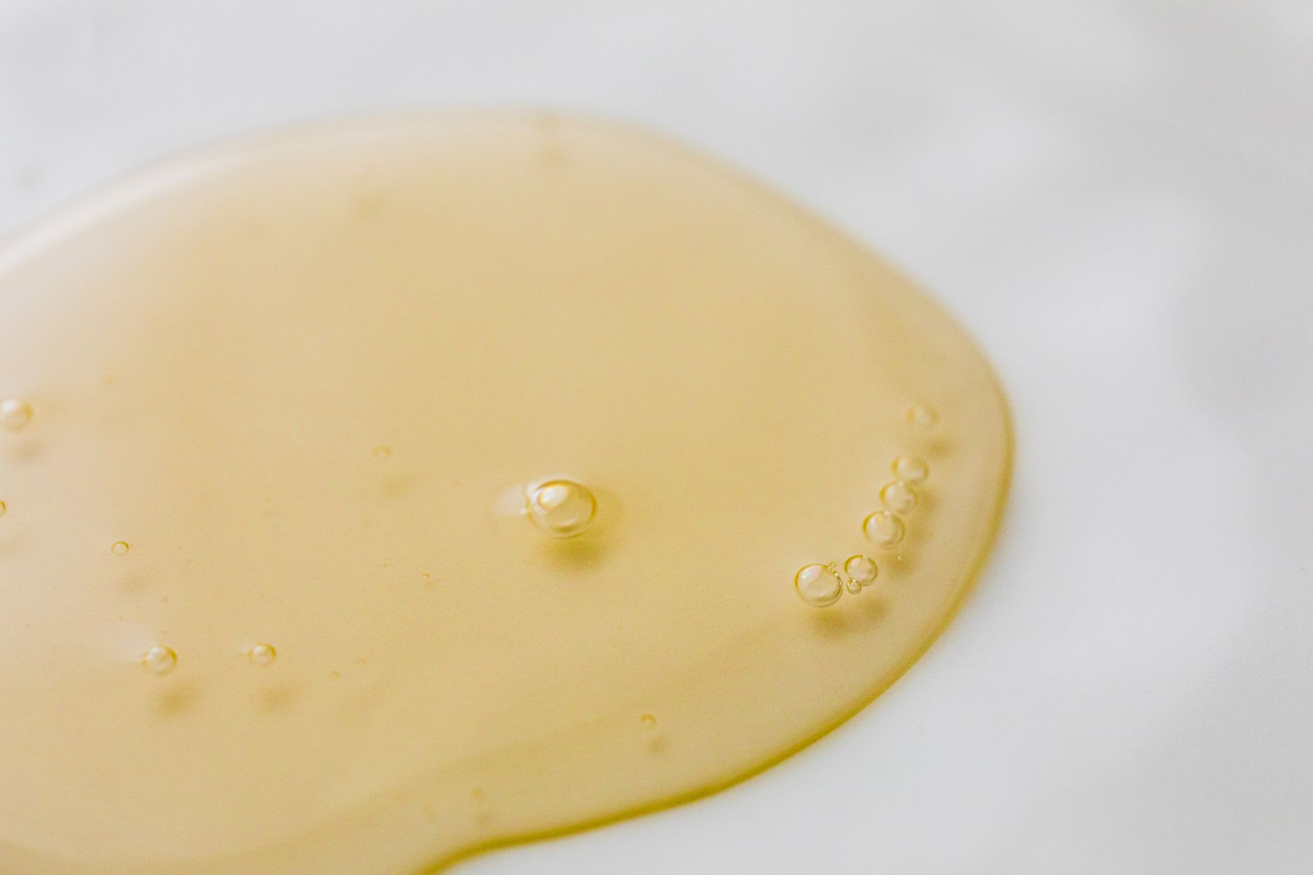 From above closeup of transparent yellowish oily substance with few bubbles on smooth white surface