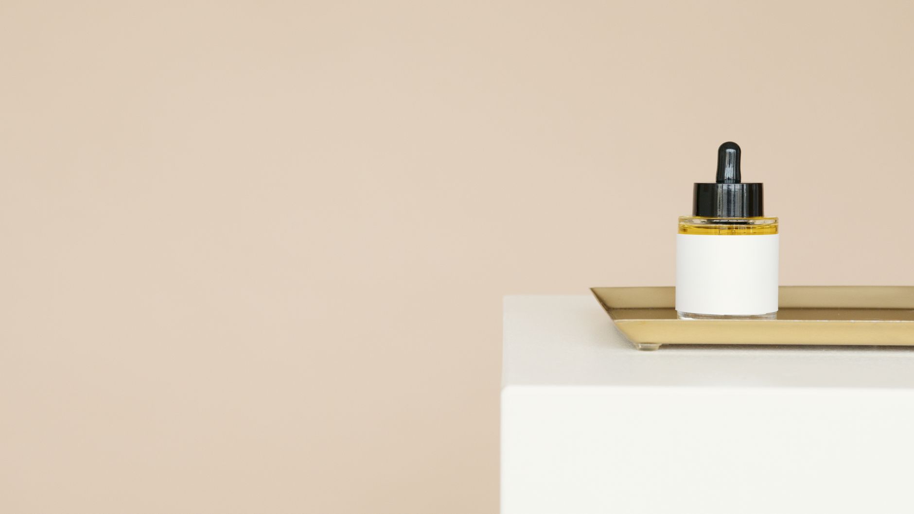 A dropper bottle of oil on a tray with a beige background, offering copy space.