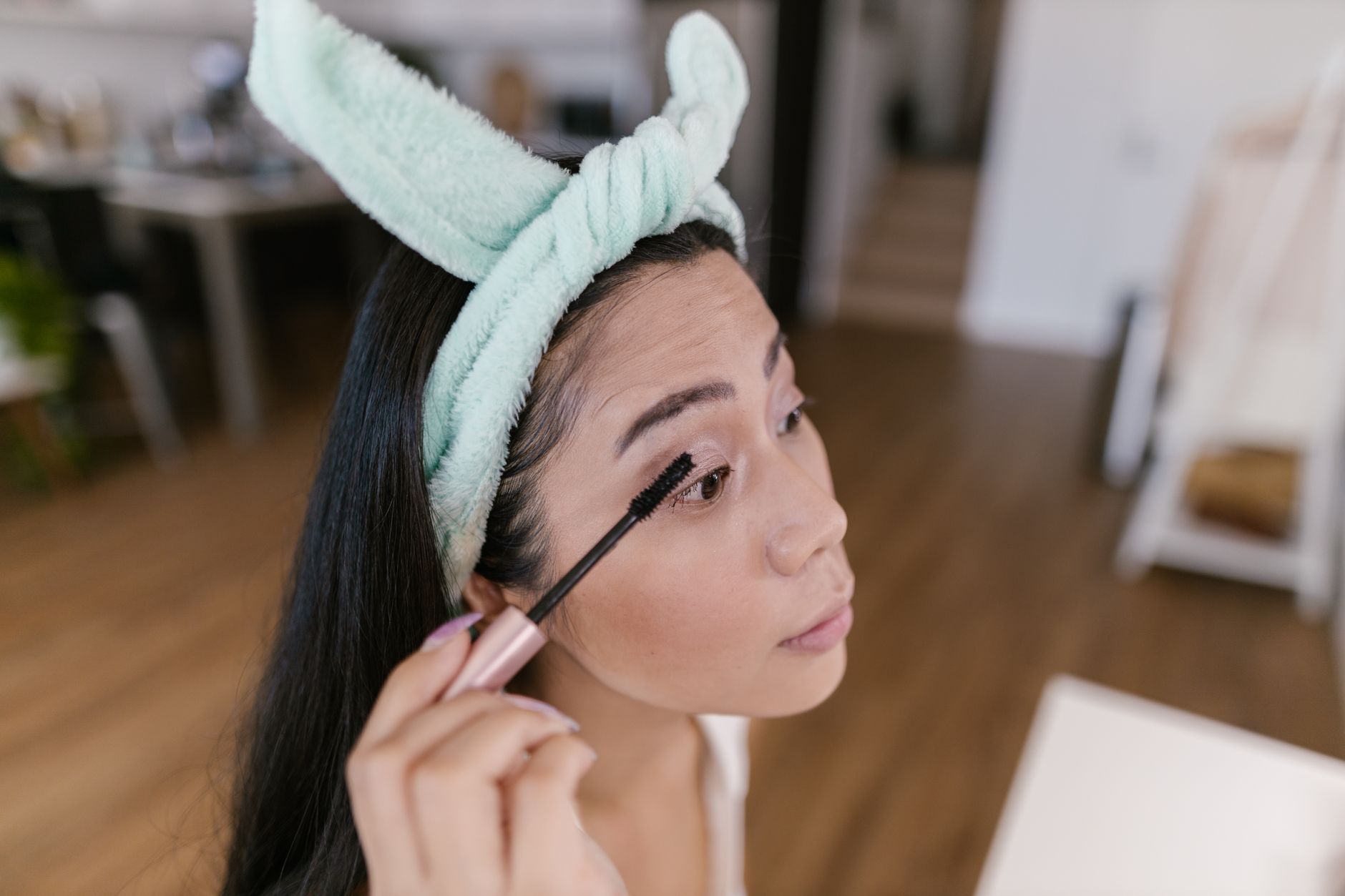 Asian woman applying mascara indoors for a natural beauty look.