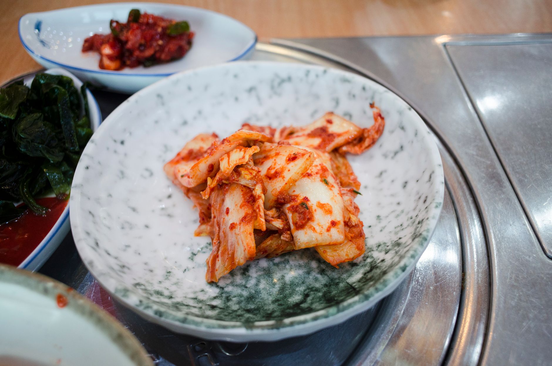 Close-up of spicy Korean kimchi served in a traditional ceramic bowl on a dining table.