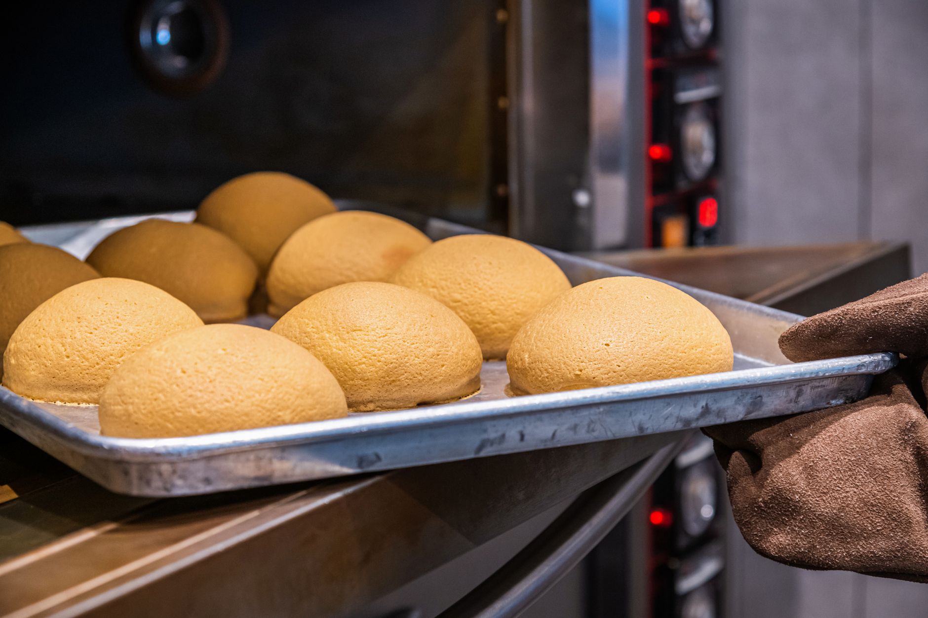 Close-up of freshly baked golden brown bread rolls on a stainless steel tray being removed from an oven.