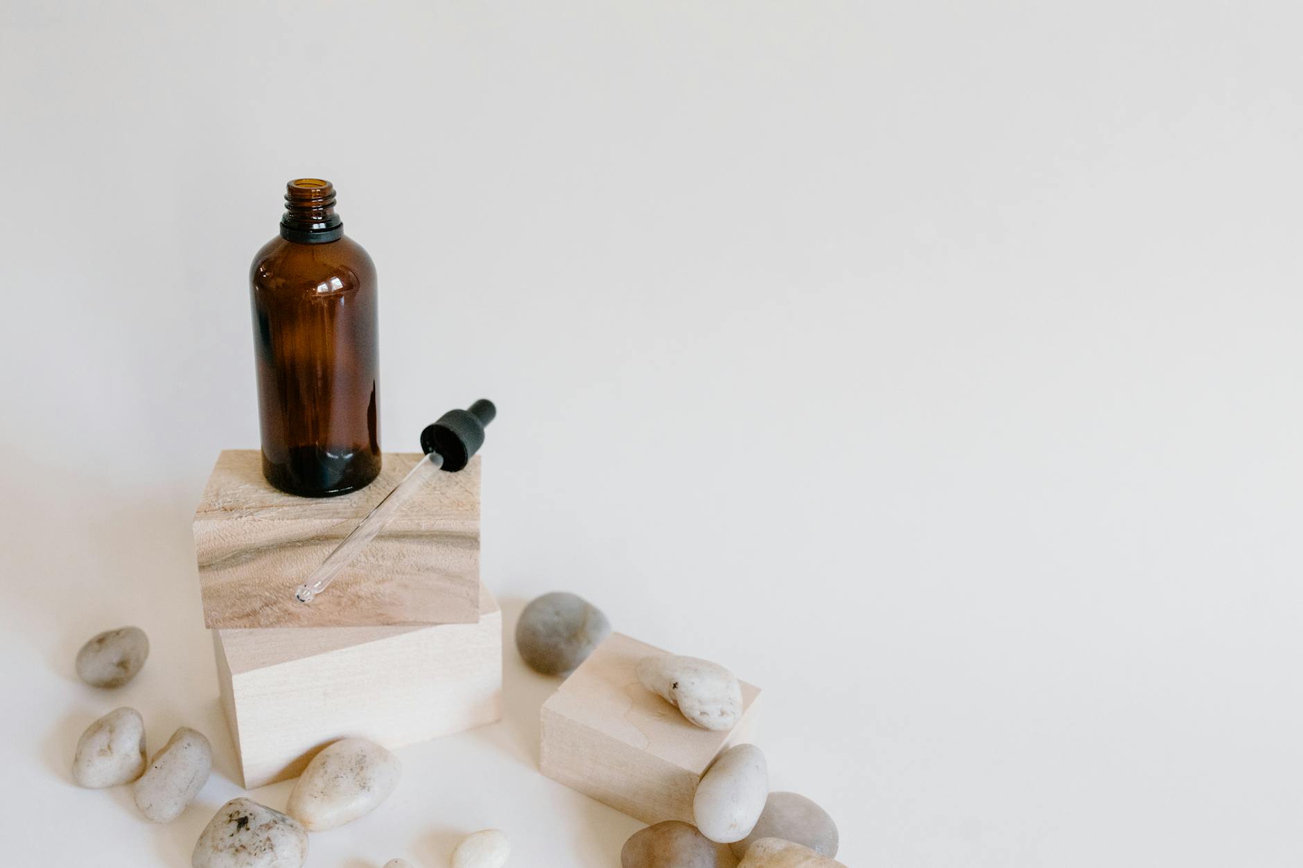 A brown glass dropper bottle on wooden blocks surrounded by stones, epitomizing serenity and natural wellness.