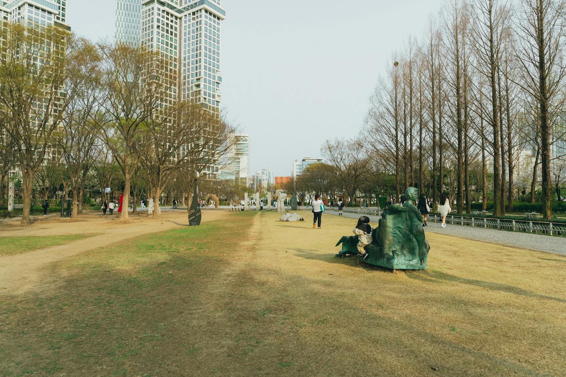 Park scene in Seoul, South Korea, featuring skyscrapers and sculptures, during a bright spring day.
