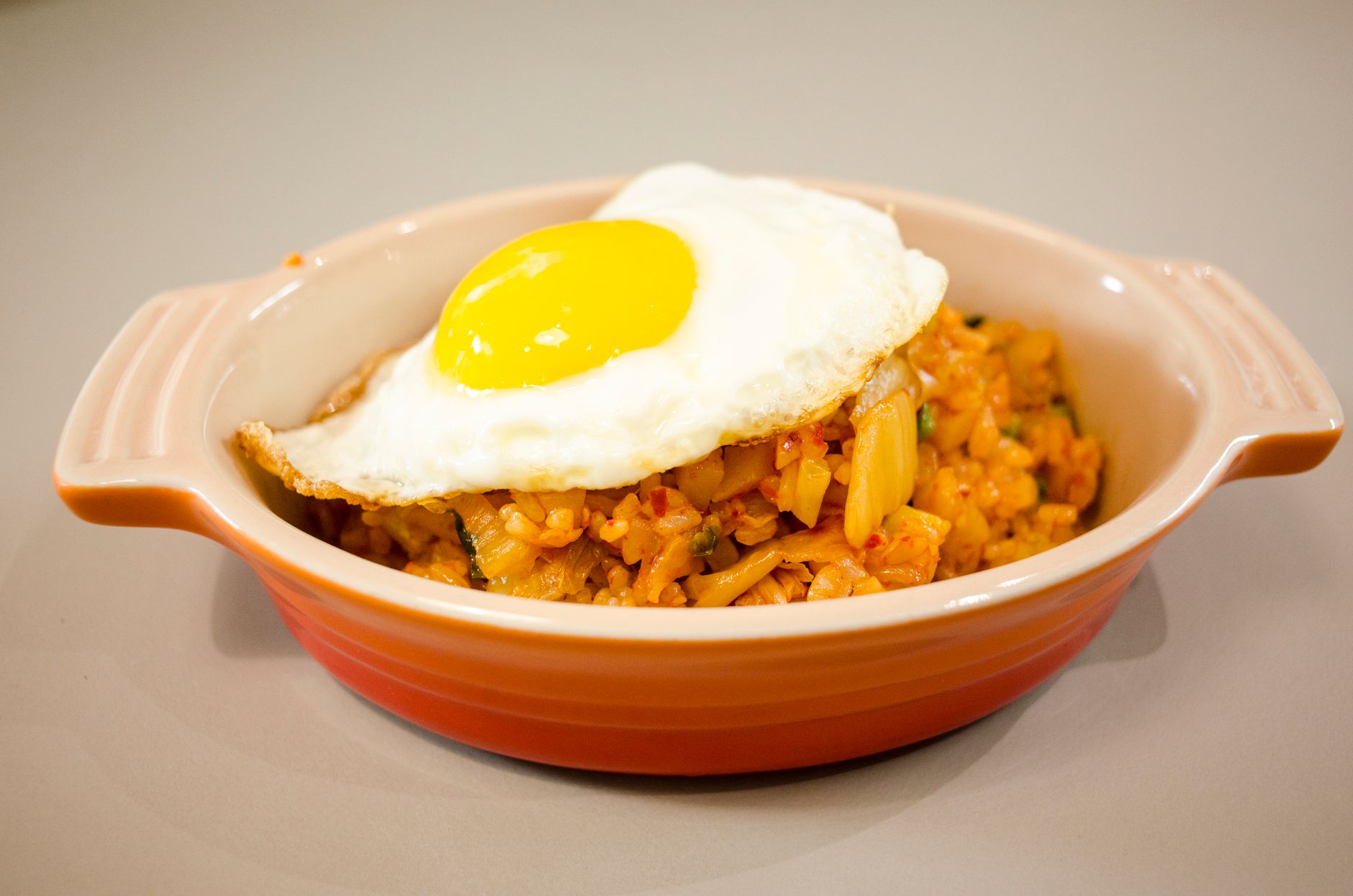 Close-up of kimchi fried rice topped with a sunny-side-up egg in a ceramic dish.