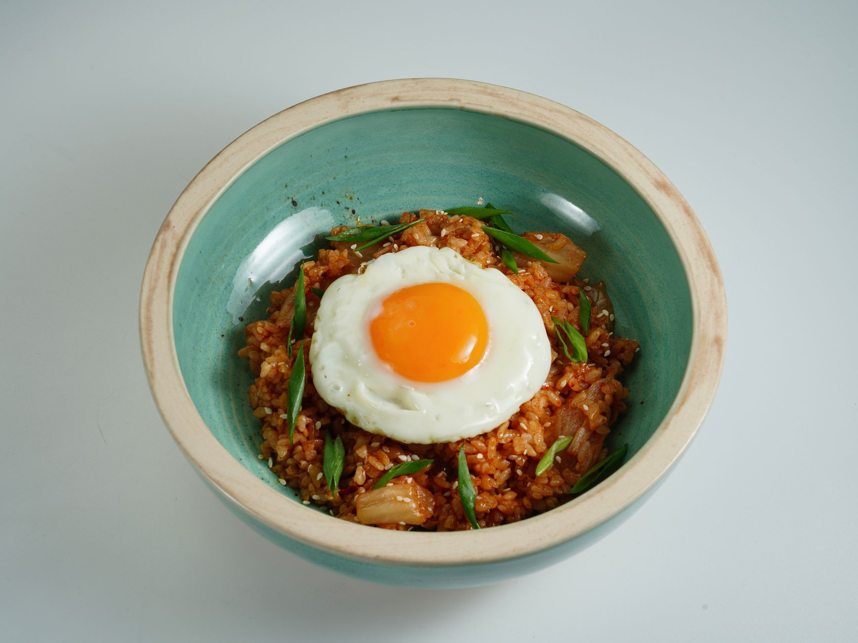 Close-up of flavorful kimchi fried rice with a sunny-side-up egg in a ceramic bowl.