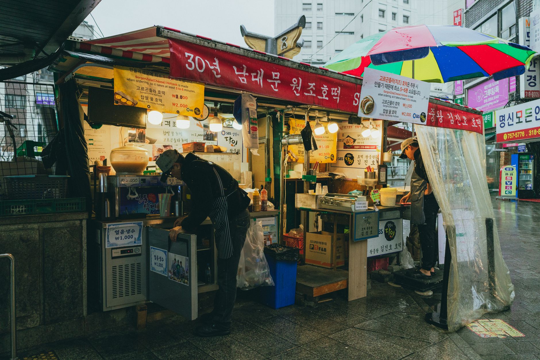 A vibrant street food stall in Seoul's rainy marketplace showcasing Korean culture and cuisine.