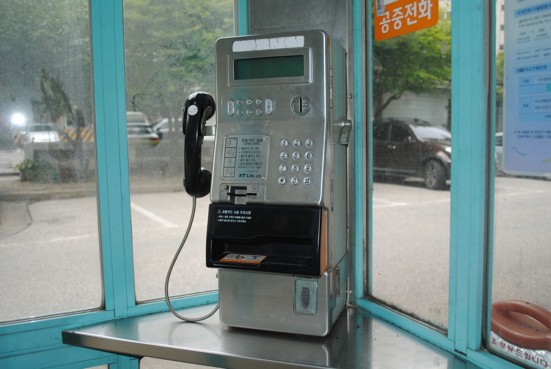 A retro public payphone inside a light blue booth in an urban outdoor setting.