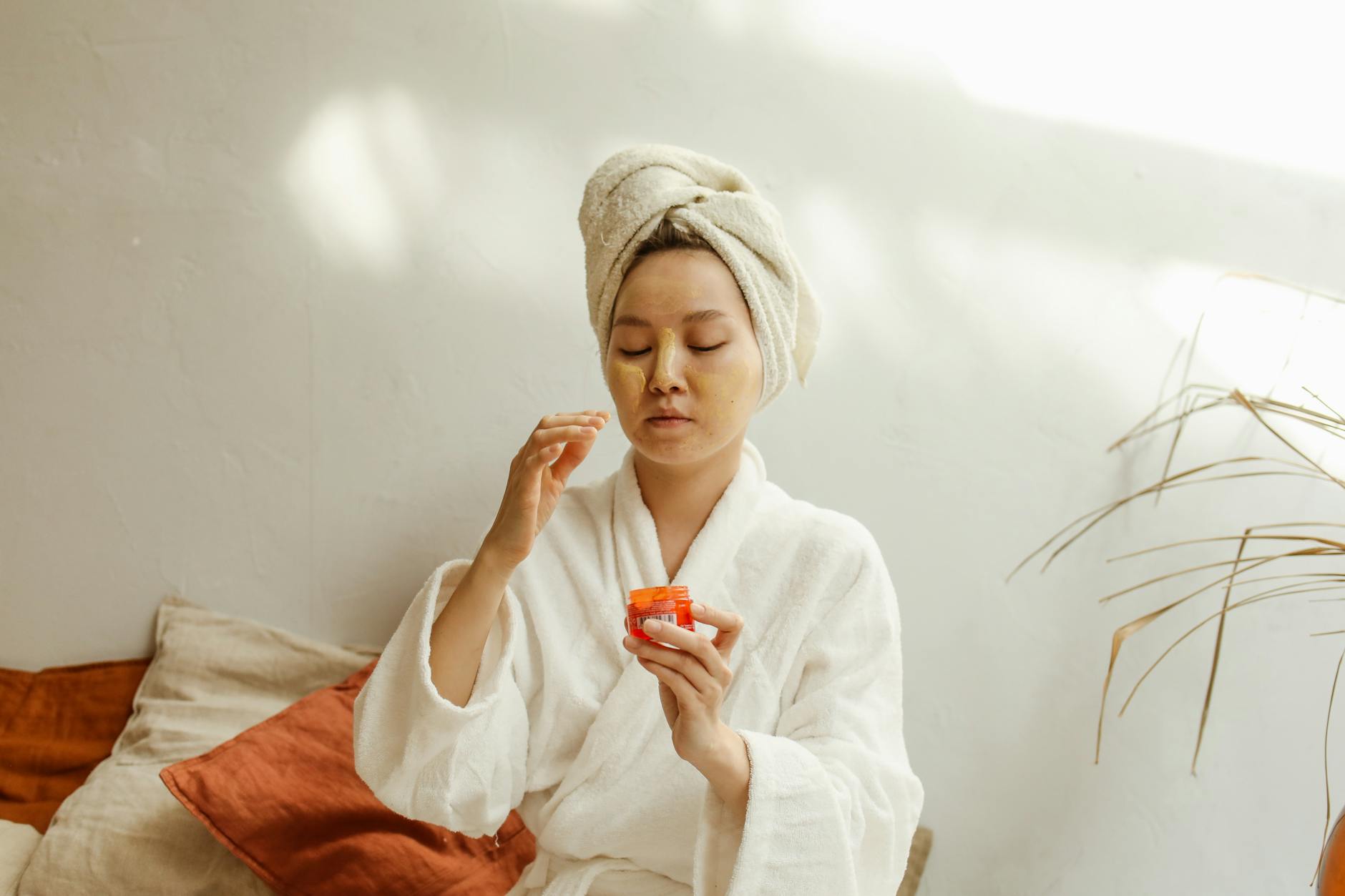 An adult Asian woman applies facial cream as part of her skincare routine indoors.