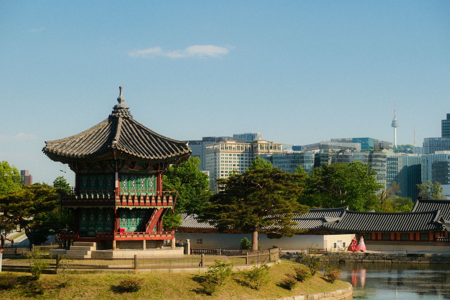 A traditional Korean pagoda in a serene park with a modern city skyline in the background, showcasing cultural contrast.