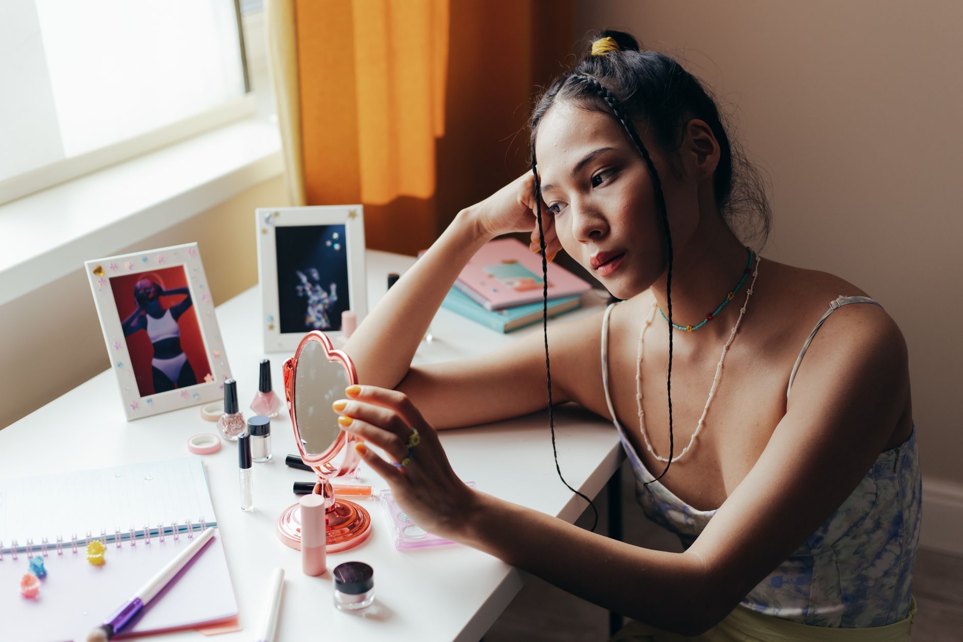 Asian woman daydreaming while using a cosmetic mirror indoors.