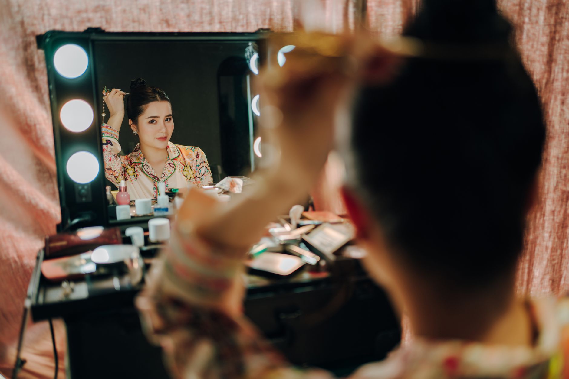 Asian woman fixing her hair in front of a makeup mirror, indoors.