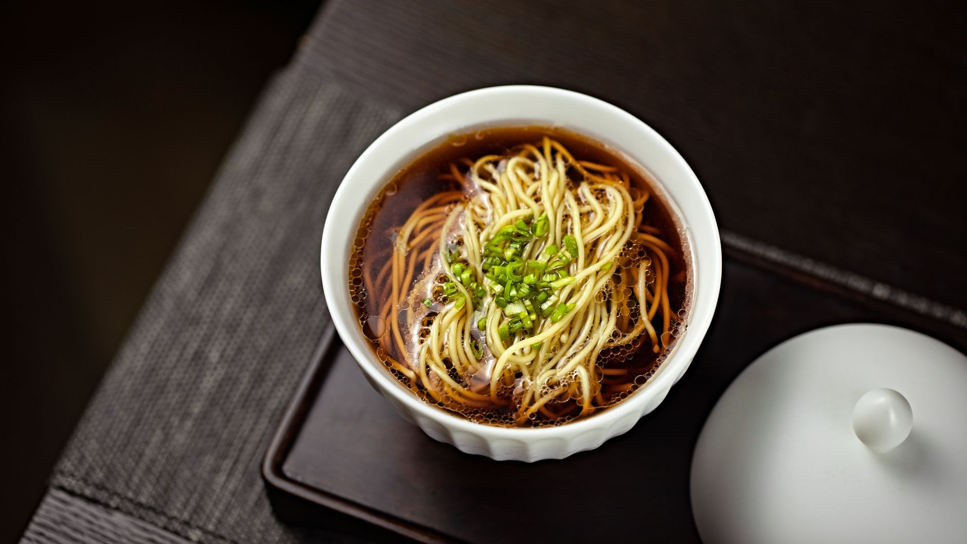 A flavorful bowl of noodles served in a savory broth, garnished with fresh green onions.