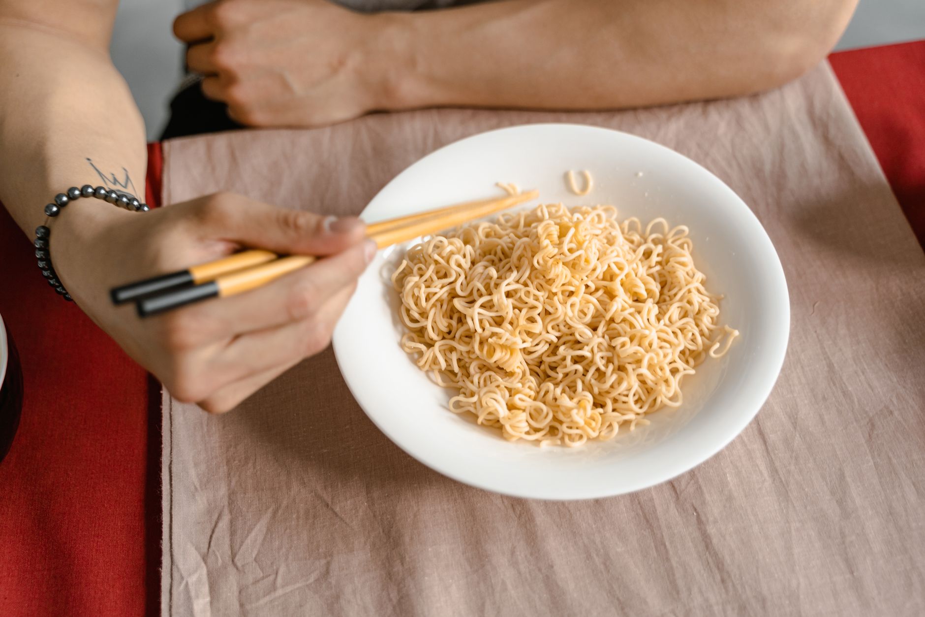 A person holding chopsticks ready to eat noodles from a white bowl at a table.