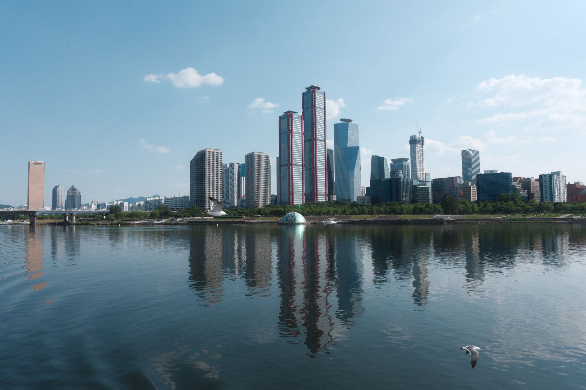 A stunning Seoul skyline reflecting in the river under a clear blue sky.
