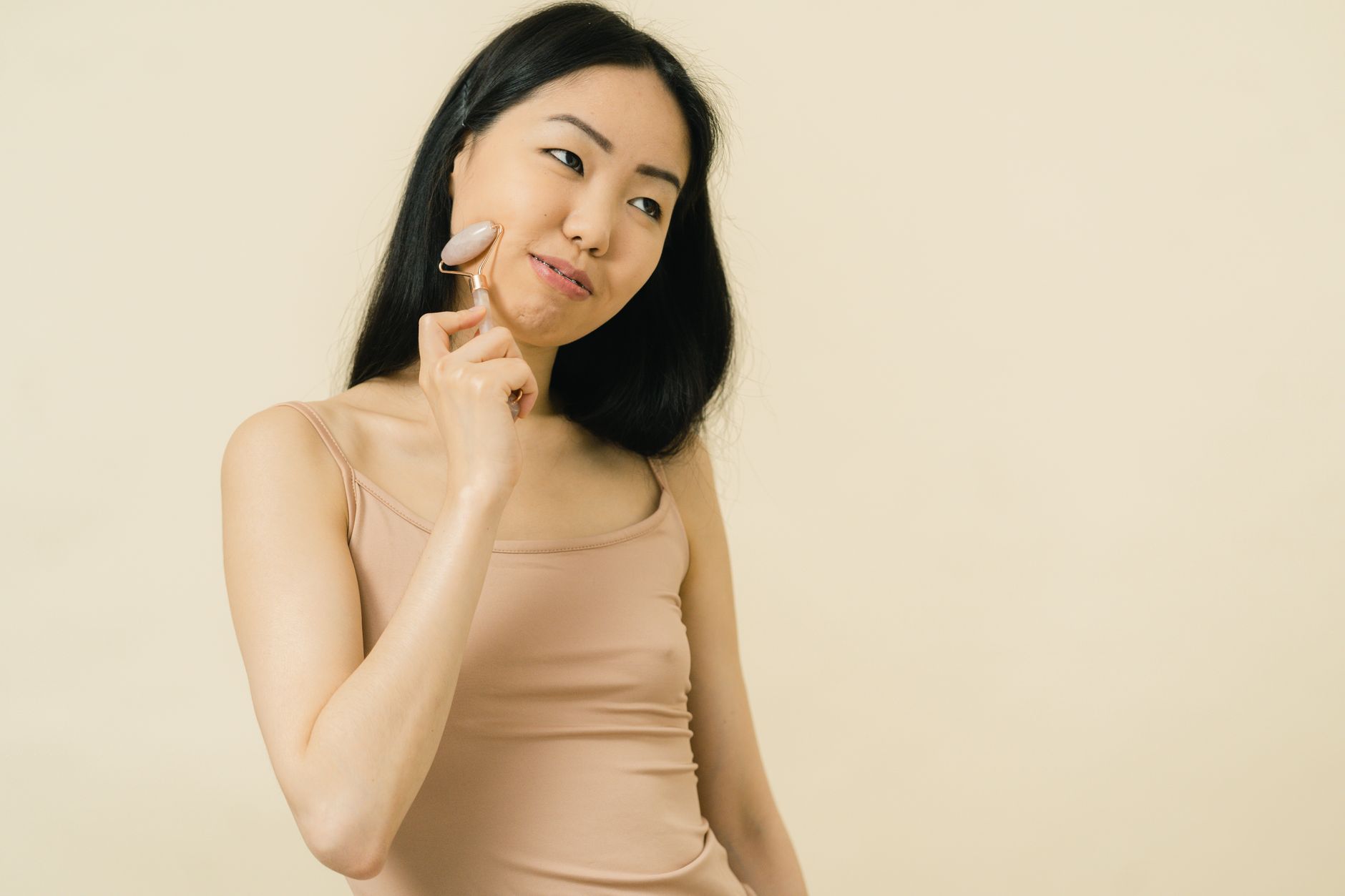 Asian woman using a gua sha roller for facial skincare in a studio setting.